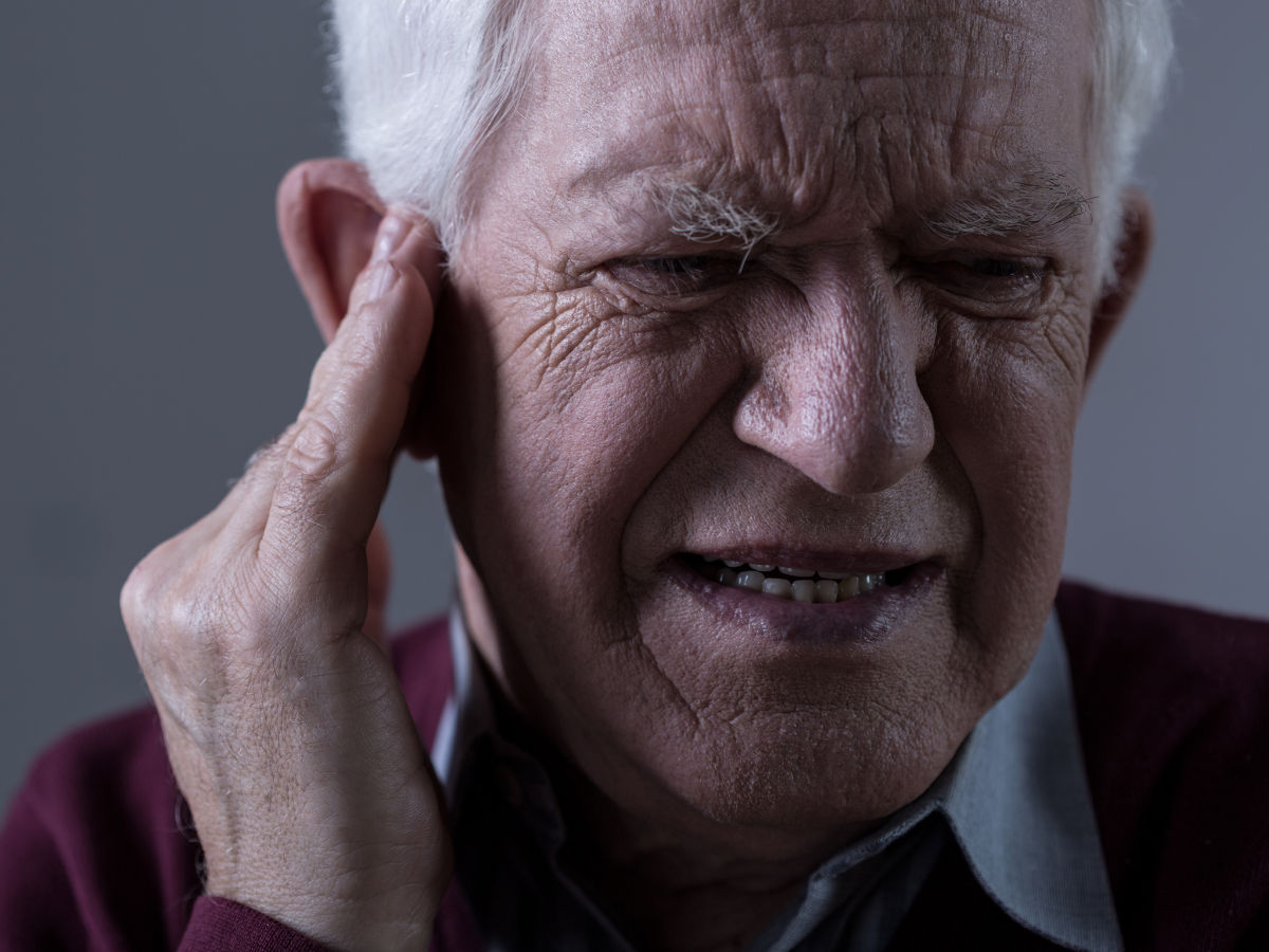 elderly man holding his ear suffering from tinnitus